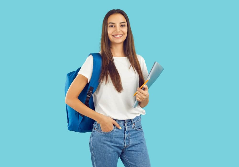 Joven estudiante con mochila y libros en fondo azul, promoviendo educación y formación académica.
